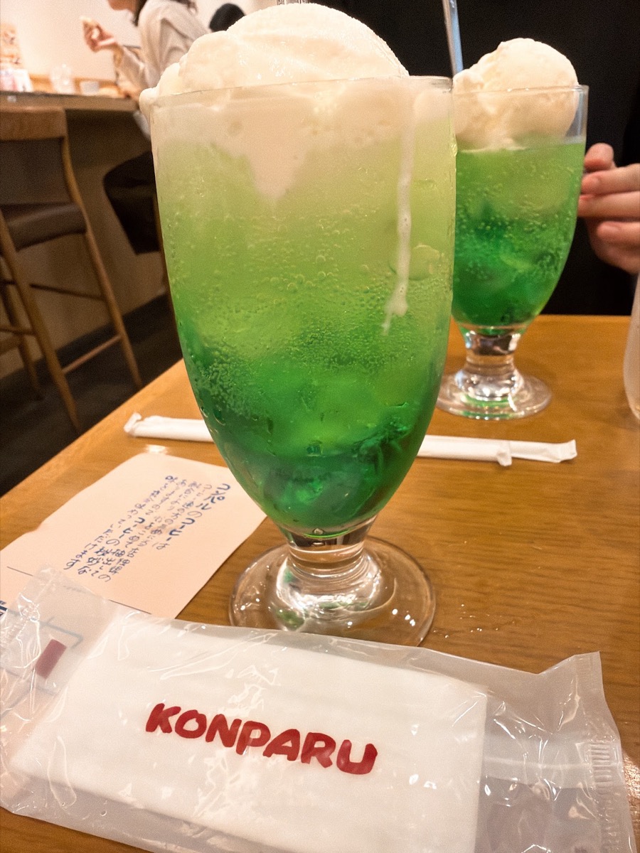 コンパル サンロード店のクリームソーダ エメラルドグリーンのメロンソーダに白いソフトクリーム KONPARUロゴ入りの紙